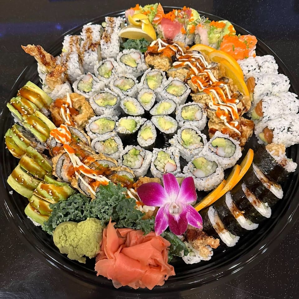 A large platter of assorted Flame Sushi rolls, including avocado, tempura, and nigiri, garnished with ginger and wasabi.