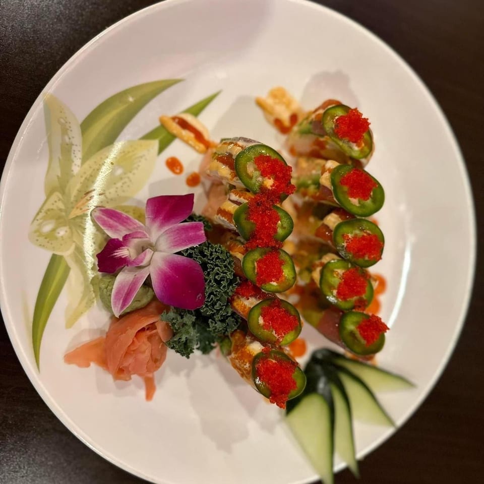 Sushi rolls topped with jalapeños and red roe, garnished with orchids, ginger, and kale.