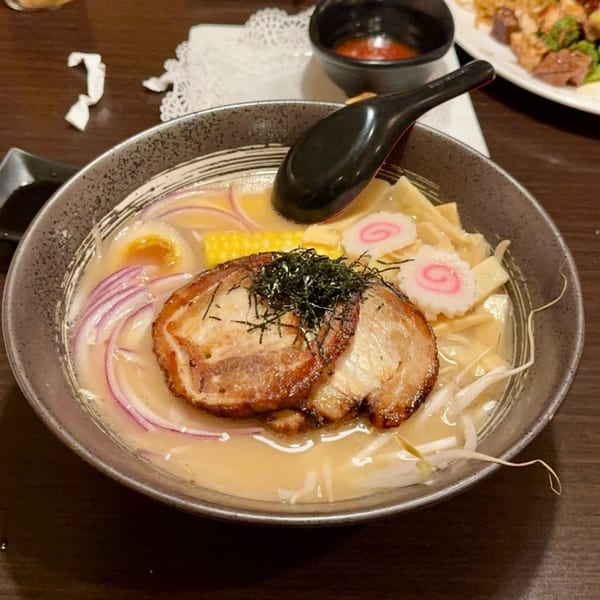 A close-up of a bowl of Flame Sushi ramen with pork, egg, corn, red onions, and fish cake.