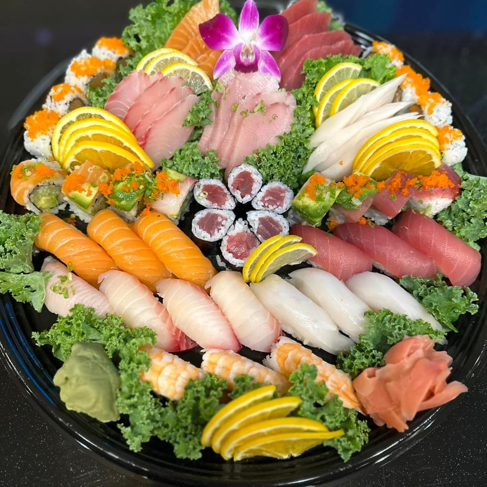 A large platter of Flame Sushi's Japanese sushi, sashimi, and rolls, garnished with lemon, orange, and a purple orchid.