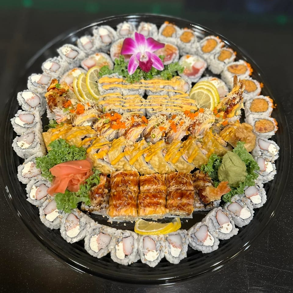 A large platter of Flame Sushi Japanese Grill's assorted sushi rolls, garnished with lemon, ginger, and an orchid.