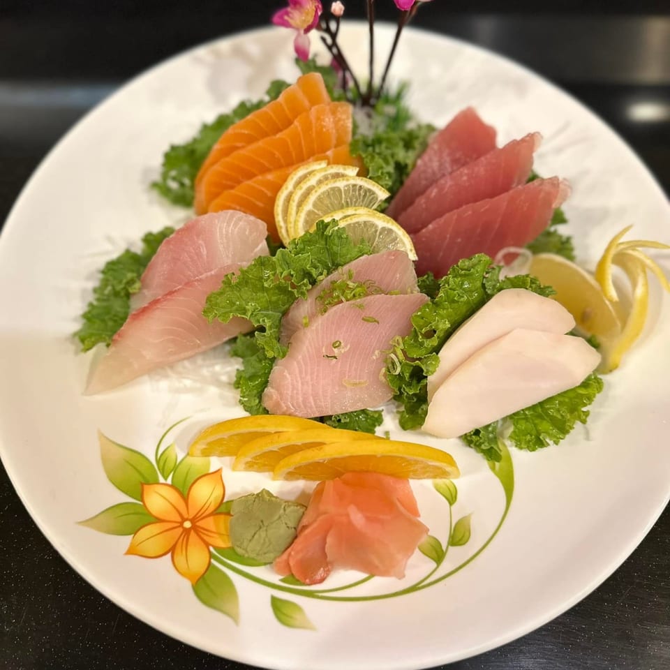 A colorful sashimi platter with various fish, lemon, orange slices, wasabi, and ginger on a white plate.